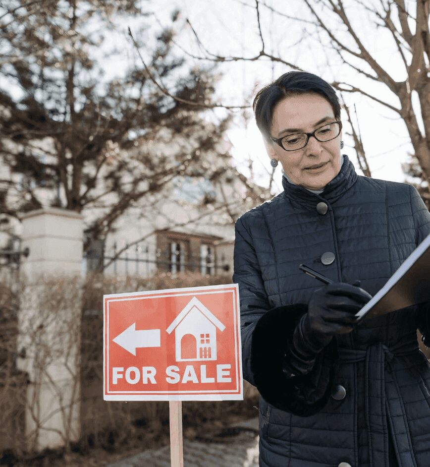 Woman with clipboard near for sale sign