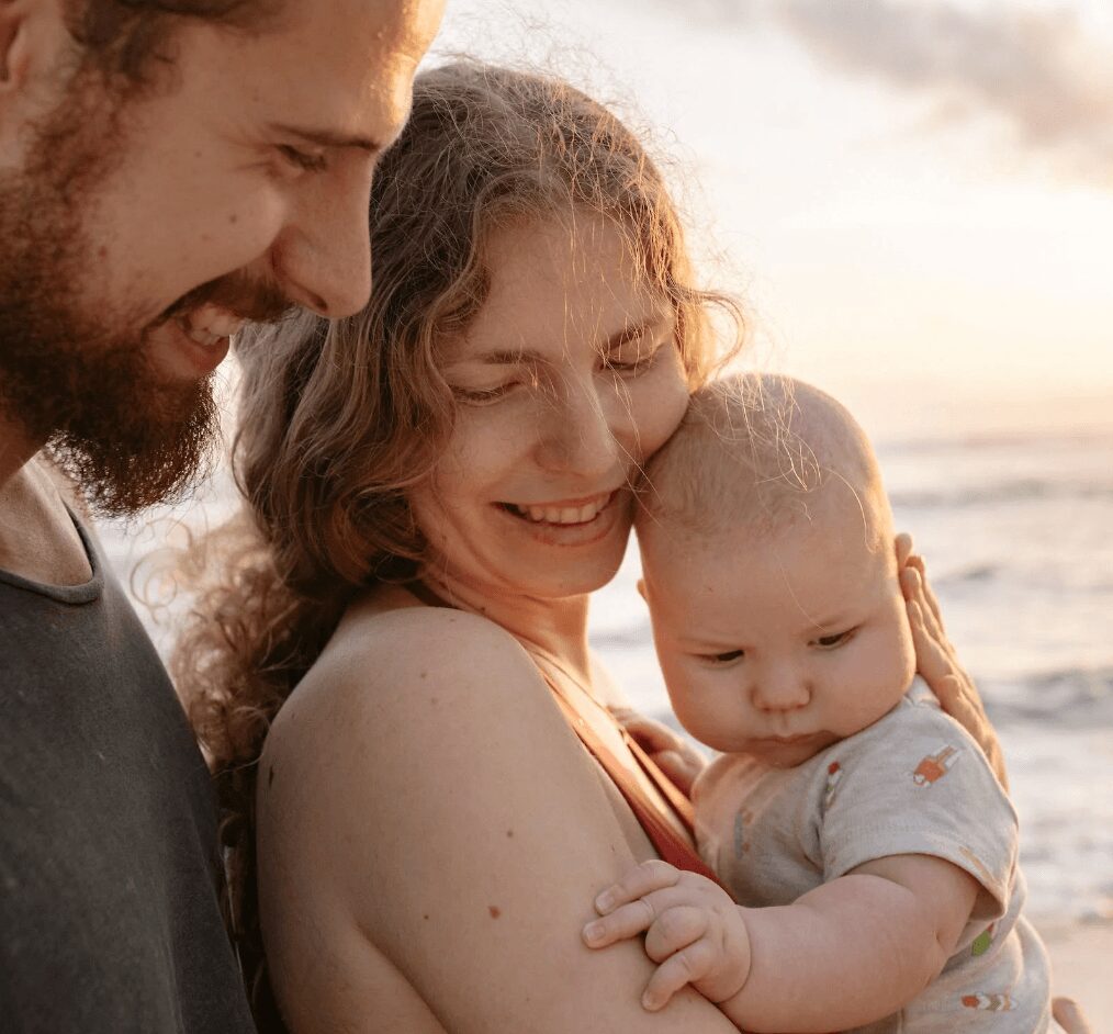 Baby held by smiling parents at sunset
