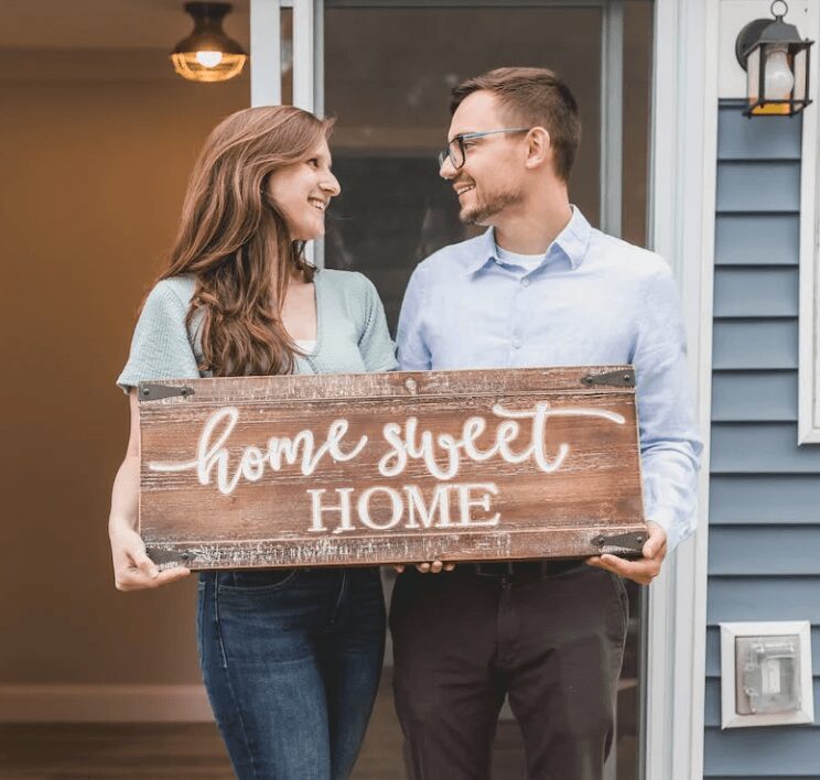 New homeowners smiling with wooden sign