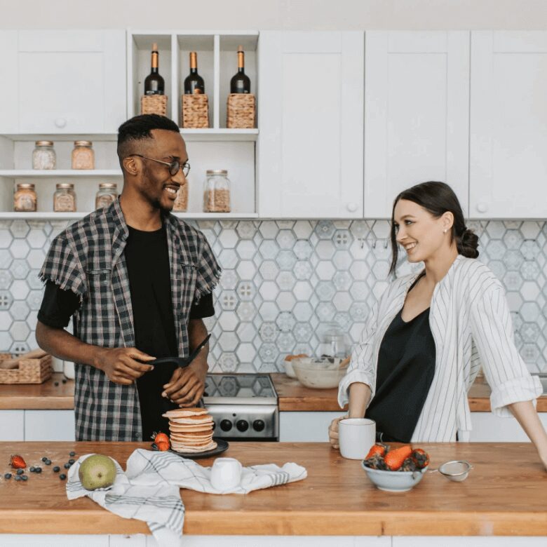 Smiling couple preparing pancakes and fruit