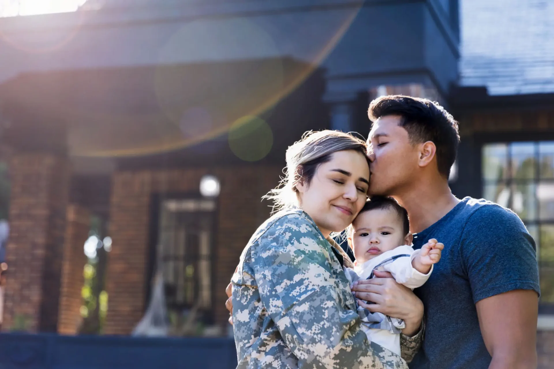 Soldier embraces family, sharing a tender moment outdoors.