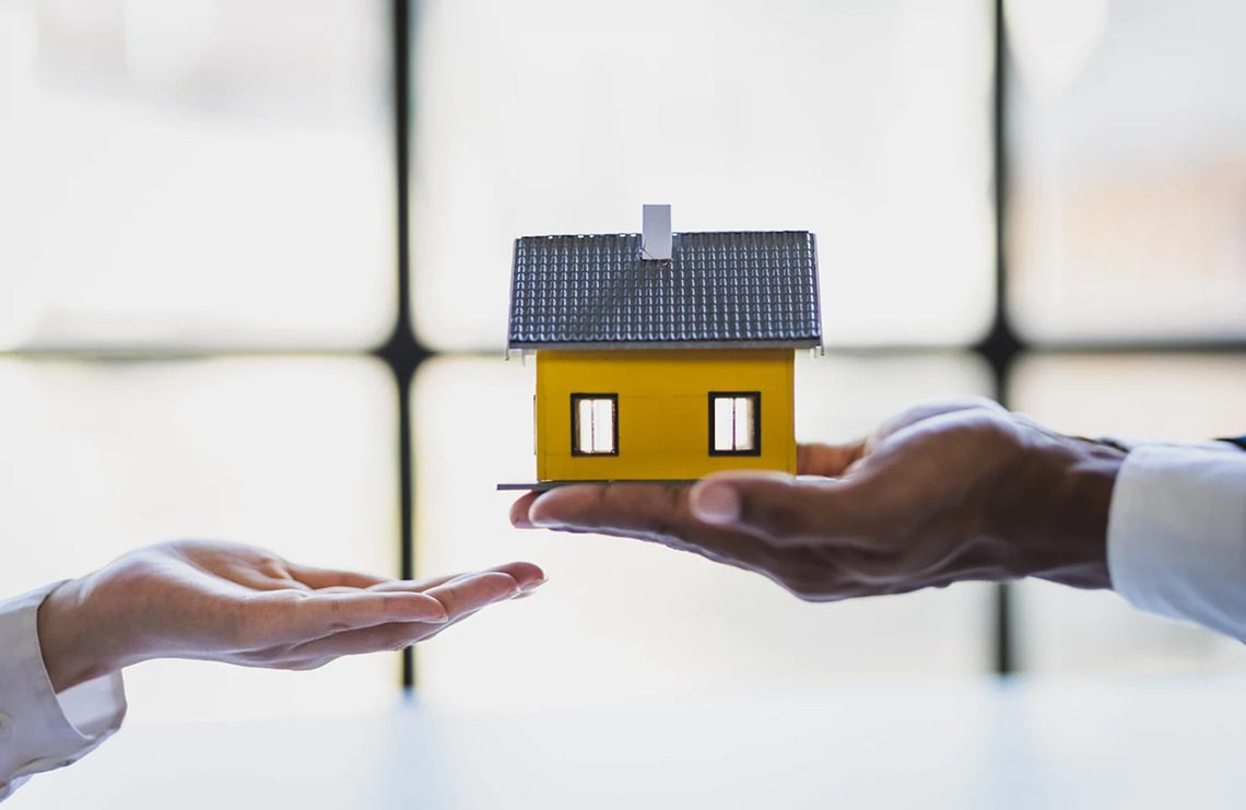 Hands holding a small yellow house model.