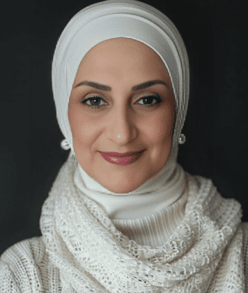 Portrait of a smiling woman wearing a white hijab and pearl earrings.